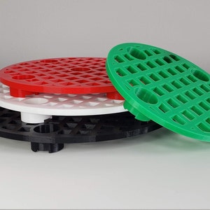 May include: Three round, plastic, stackable trays with a grid pattern. The top tray is green, the middle tray is white, and the bottom tray is black.
