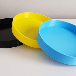 Peut inclure: Trois plateaux ronds en plastique, un noir, un jaune et un bleu.