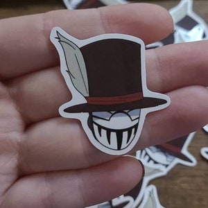 Puede incluir: Un conjunto de pegatinas en blanco y negro con un personaje de dibujos animados con un sombrero de copa y una sonrisa amenazante. El personaje tiene una pluma en el lateral de su sombrero.