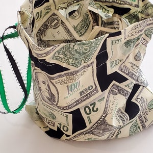 May include: A black drawstring bag with a green and black drawstring. The bag is made of fabric and has a pattern of US dollar bills.