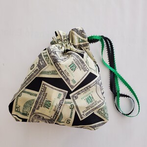 May include: A black drawstring bag with a green and black drawstring. The bag is printed with images of US dollar bills.