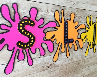 May include: A pink, orange, and yellow slime themed party banner with the word "SLIME" spelled out in black letters with yellow polka dots.
