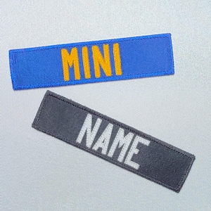 May include: Two rectangular patches. The top patch is blue with the word "MINI" embroidered in yellow. The bottom patch is gray with the word "NAME" embroidered in white. Both patches are rectangular.