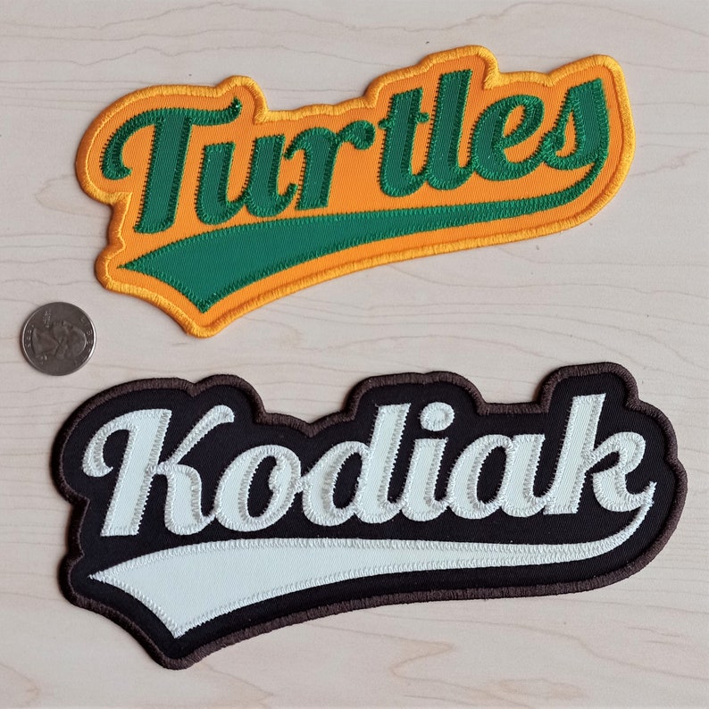 May include: Two embroidered patches with a baseball-style font. The top patch is yellow with green lettering that says "Turtles". The bottom patch is brown with white lettering that says "Kodiak".