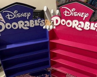 May include: Two display shelves, one blue and one pink, with the Disney Doorables logo. Each shelf has multiple levels for displaying items. The top of each shelf has a house-shaped design.