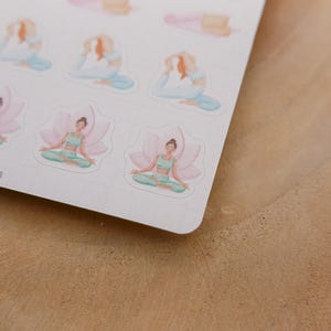 May include: A sheet of stickers featuring watercolor illustrations of yoga poses. The stickers depict figures in various yoga positions, including seated lotus and reclining poses, in soft pastel colors. The stickers are on a white background.