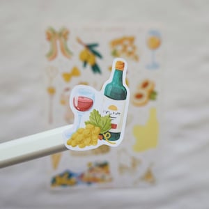 May include: A sticker featuring a wine bottle, a glass of red wine, and a bunch of grapes. The bottle is green with a yellow label. The glass is filled with red wine. The grapes are yellow. The sticker is held by a white stylus.