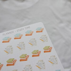 May include: A sheet of planner stickers with a study theme. The stickers feature stacks of books in orange, green, and blue, along with pencils and notepaper. The text "PLANNER - STUDY TIME" is printed at the top.