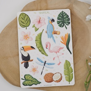 May include: A rectangular sticker sheet titled TROPICAL featuring illustrations of a blue parrot, a pink flamingo, a toucan, a dragonfly, a coconut, various tropical leaves, and flowers including hibiscus and plumeria on a white background.