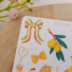 May include: A sticker sheet with Italian summer-themed illustrations. The sheet features a bow with orange, green, and white stripes, olive branch, pasta, and the text "ITALIAN SUMMER".