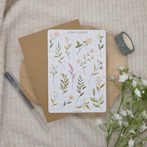 May include: A rectangular sticker sheet titled DAINTY FLOWERS featuring various botanical illustrations of wildflowers, leaves, and stems in muted green, pink, and yellow tones, set against a white background with small geometric shapes.
