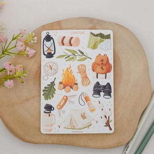 May include: A rectangular sticker sheet titled CAMPING featuring various illustrations including a lantern, rolled sleeping bag, map, compass, campfire, rope, backpack, binoculars, oak leaf, pocket knife, flashlight, tent, and thermos.