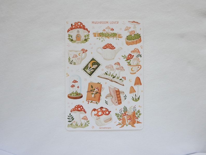 May include: A sticker sheet titled MUSHROOM LOVER featuring various illustrations of mushrooms, including a mushroom house, a teapot, mugs, books, and a glass dome. The designs are rendered in earthy tones of red, brown, green, and cream on a white background.