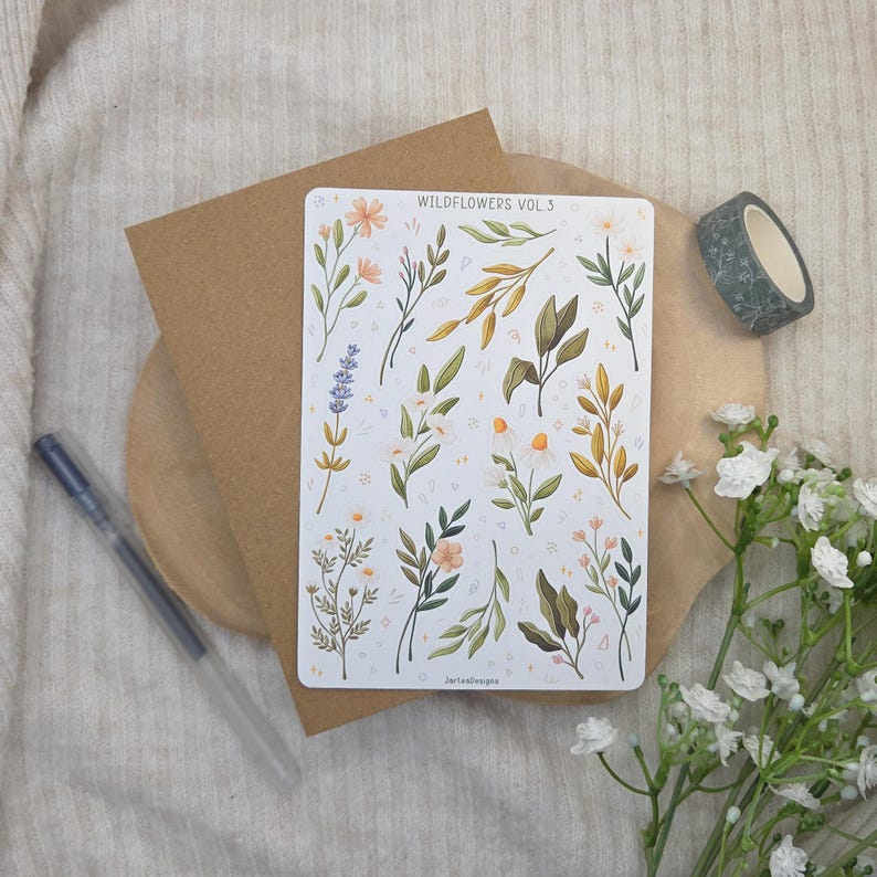 May include: A rectangular sticker sheet titled WILDFLOWERS VOL 3 featuring various botanical illustrations of lavender, daisies, and leafy stems in muted green, yellow, and purple tones, arranged on a white background with small decorative shapes.