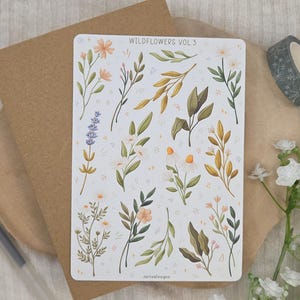 May include: A rectangular sticker sheet titled WILDFLOWERS VOL 3 featuring various botanical illustrations including lavender, daisies, and leafy branches in shades of green, yellow, and soft orange, accented with small white star and dot patterns.