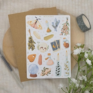 Puede incluir: Una hoja de pegatinas rectangular titulada WITCHCRAFT que presenta varias ilustraciones que incluyen una polilla, cristales, hierbas secas, una calavera, cartas del tarot, frascos de pociones, una planchette, una bola de cristal y velas.