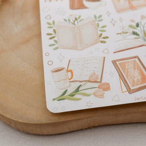 Peut inclure: Une planche d'autocollants illustrant des livres ouverts, des plantes en pot, des tasses &agrave; caf&eacute; et des cadres dans des tons beige et vert doux. Les motifs incluent des &eacute;l&eacute;ments floraux, des croquis botaniques et le texte JarteaDesigns.
