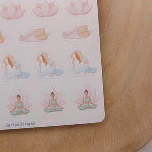 May include: A sheet of watercolor stickers featuring yoga poses, lotus flowers, and yoga mats. The stickers are in soft pastel colors, including pink, blue, and green. The text "JarteaDesigns" is printed on the bottom of the sticker sheet.