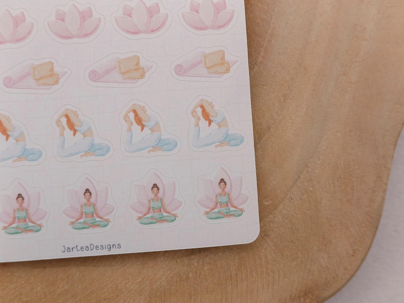 May include: A sheet of watercolor stickers featuring yoga poses, lotus flowers, and yoga mats. The stickers are in soft pastel colors, including pink, blue, and green. The text "JarteaDesigns" is printed on the bottom of the sticker sheet.