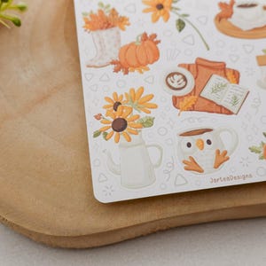 May include: A sheet of fall-themed stickers featuring pumpkins, sunflowers, coffee, and a sweater. The stickers have a white background with a variety of fall-related illustrations. The text "JarlesDesigns" is visible on the bottom right of the sticker sheet.
