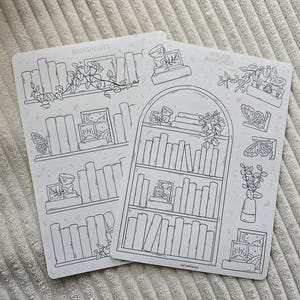 May include: Two white sticker sheets with bookshelf and botanical illustrations. One sheet reads "Bookshelves" and the other reads "Tracker Bookshelf". The designs include books, plants, butterflies, and framed art, all in a line drawing style.