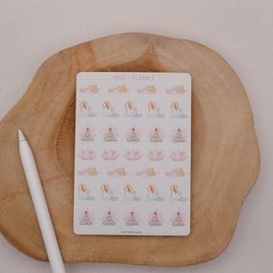 May include: A sheet of yoga planner stickers featuring various yoga poses in pastel colors. The stickers are on a white background with the text "YOGA + PLANNER". A white stylus pen rests on a wooden surface.