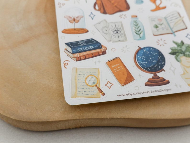 May include: A sticker sheet featuring various illustrations including a blue spellbook, a magnifying glass over a document, a celestial globe, tarot cards, a moth in a glass dome, and a potted plant, with the text www.etsy.com/shop/JarteaDesigns.
