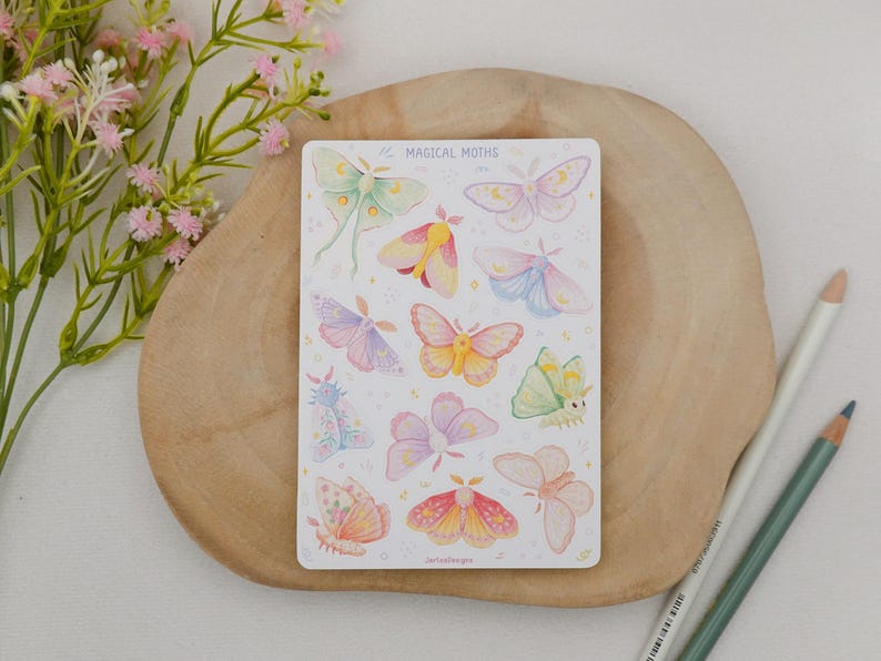 May include: A rectangular sticker sheet titled MAGICAL MOTHS featuring various pastel-colored moth illustrations in shades of pink, yellow, blue, and green. The moths are arranged in a grid pattern with small star accents on a white background.