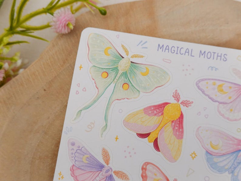 May include: A sticker sheet titled MAGICAL MOTHS featuring watercolor illustrations of various moths in pastel shades of green, pink, yellow, and purple. Each moth is decorated with small crescent moon and circular patterns on its wings.