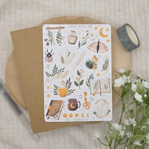 May include: A rectangular sticker sheet titled Forest Witch featuring various illustrations including a beetle, crystals, a moth, a potion bottle, a book, a key, a mug, and moon phases in earthy tones of brown, green, yellow, and soft pink on a white background.