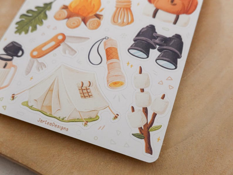 May include: A sticker sheet featuring camping-themed illustrations including a white tent, a campfire, a multi-tool, a flashlight, binoculars, and marshmallows on a stick. The text JarteaDesigns is printed in brown near the bottom left corner.