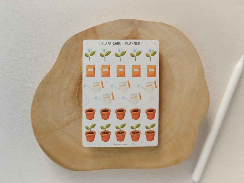 May include: A sticker sheet with a plant care planner design. The sheet features illustrations of watering cans, seed packets, potted plants, and sprouting plants. The text "PLANT CARE - PLANNER" is at the top. The sticker sheet is on a wooden surface.