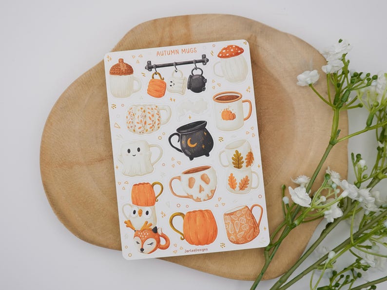 May include: A sticker sheet with illustrations of autumn-themed mugs. The mugs have designs such as pumpkins, acorns, and woodland creatures. The color scheme is warm, with orange, brown, and cream tones. The text "AUTUMN MUGS" is displayed at the top of the sheet.