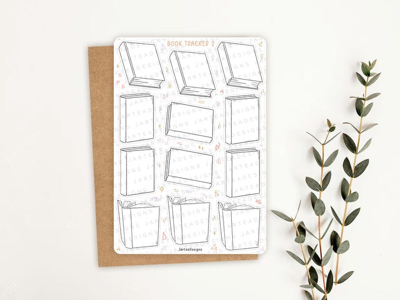May include: A white sticker sheet with the text "Book Tracker 2" and outlines of books. The sticker sheet is on a brown card with a white background and a sprig of green leaves.