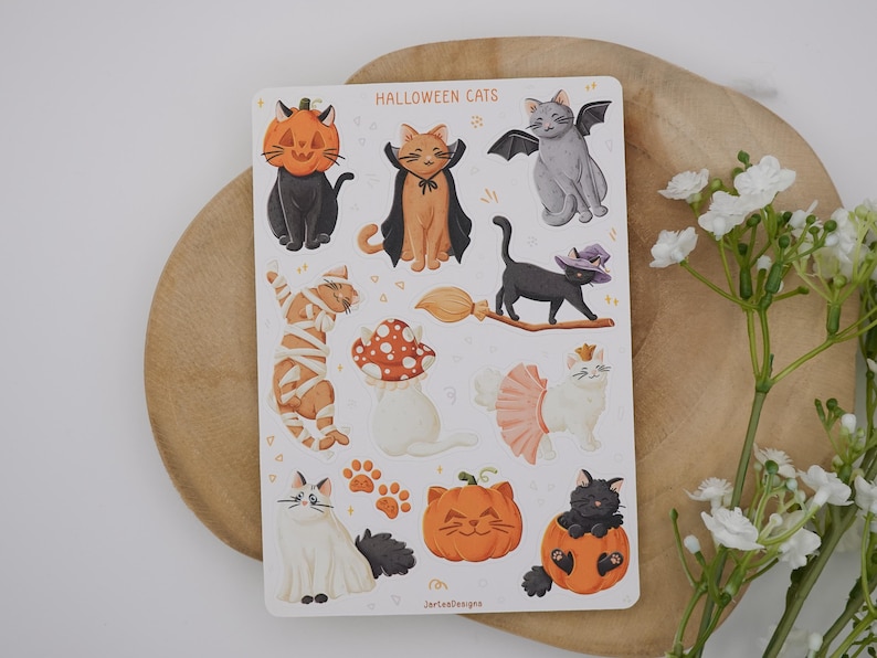 Pu&ograve; includere: Un foglio di adesivi intitolato HALLOWEEN CATS con varie illustrazioni di gatti in costume, tra cui un gatto in una zucca, un gatto mummia, un gatto con ali di pipistrello, un gatto con cappello da strega su una scopa e un gatto in tut&ugrave;.