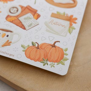 May include: A sheet of stickers featuring autumn-themed illustrations. The stickers include pumpkins, a mug with an owl design, a stack of books, and the word "Autumn". The stickers are on a white background.
