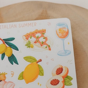 May include: A sticker sheet with illustrations of Italian summer elements. The sheet includes images of pizza, olives, lemons, peaches, and a glass of orange-colored beverage. The words "ITALIAN SUMMER" are printed at the top in light pink.