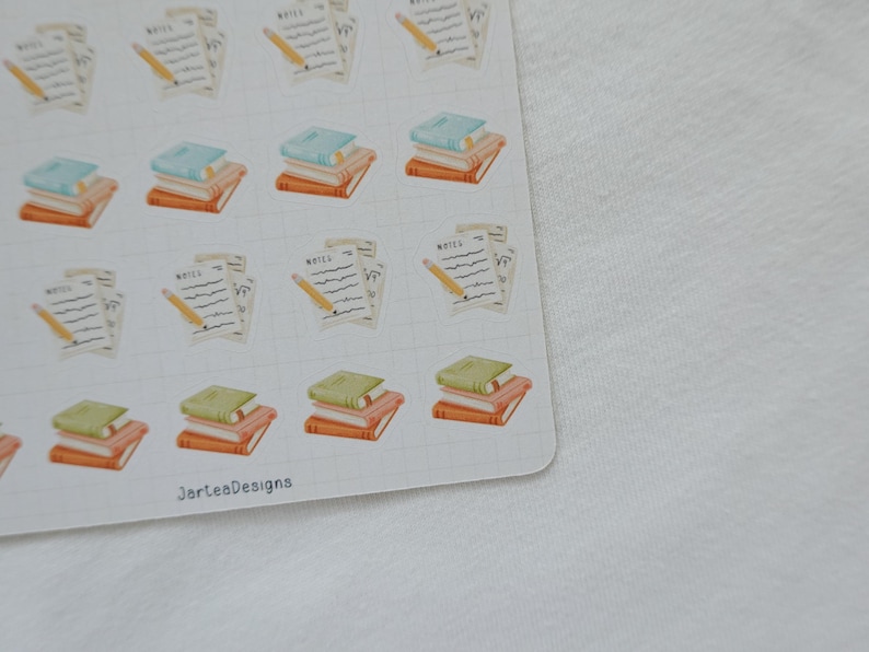 May include: A sheet of stickers featuring illustrations of books, notepads, and pencils. The books have green, blue, and orange covers. The notepads have the word "NOTES" written on them, and the pencils are yellow.