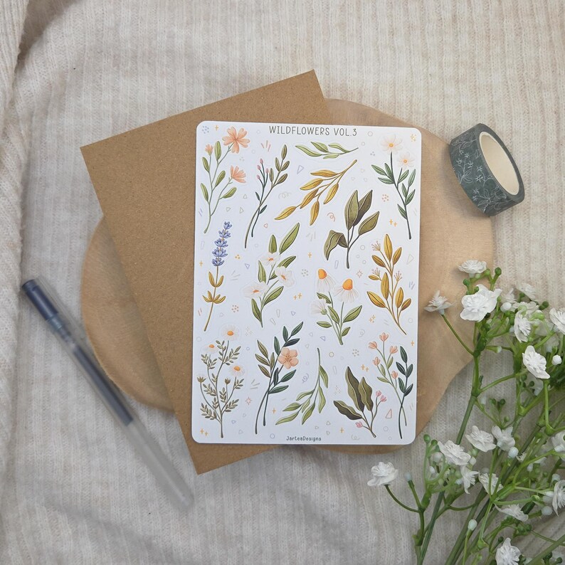 May include: A rectangular sticker sheet titled WILDFLOWERS VOL 3 featuring various botanical illustrations of lavender, daisies, and leafy stems in muted green, yellow, and purple tones, arranged on a white background with small decorative shapes.