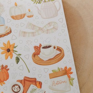 May include: A sheet of autumn-themed stickers featuring watercolor illustrations. The designs include pumpkins, candles, a scarf, a teapot, coffee cups, and fall foliage. The word "Autumn" is written on a calendar.