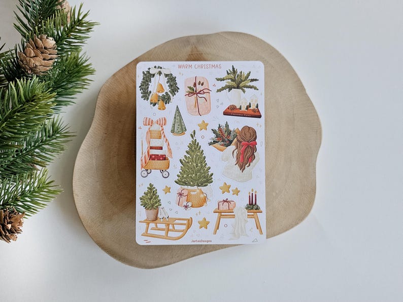 May include: A rectangular sticker sheet titled WARM CHRISTMAS featuring various holiday illustrations including a wreath, wrapped gifts, a Christmas tree, a wooden sled, a person with a red hair bow, and candles, all rendered in a soft, watercolor style.