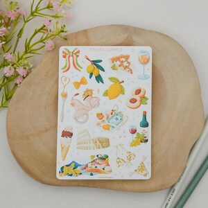May include: A sticker sheet with the words "Italian Summer" features illustrations of Italian icons. Images include a scooter, lemons, pizza, wine, gelato, the Colosseum, and a bikini. The sticker sheet is on a wooden surface with pencils and flowers.