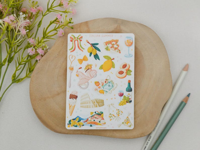 May include: A sticker sheet with the words "Italian Summer" features illustrations of Italian icons. Images include a scooter, lemons, pizza, wine, gelato, the Colosseum, and a bikini. The sticker sheet is on a wooden surface with pencils and flowers.