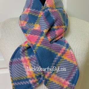 May include: A blue, pink, and yellow plaid fleece neck warmer. The neck warmer is folded in a figure eight shape and is displayed on a white mannequin.