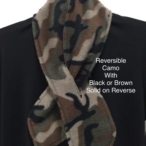 May include: Reversible camo scarf with black or brown solid on the reverse side. The scarf features a camouflage pattern in shades of green, brown, and black. The edges are stitched with a contrasting thread. The text on the image reads: Reversible Camo With Black or Brown Solid on Reverse.