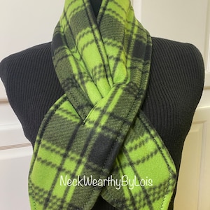 May include: A green and black plaid fleece neck warmer. The neck warmer is folded in half and is displayed on a black mannequin. The text "NeckWearthyByLois" is visible on the neck warmer.