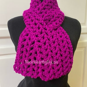 May include: A bright magenta crocheted scarf with a textured pattern. The scarf is displayed on a black mannequin.