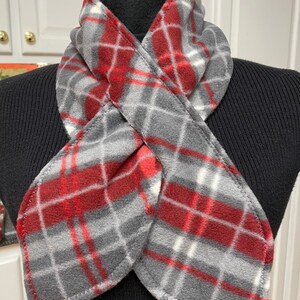 May include: A red and gray plaid fleece neck warmer. The neck warmer is folded in half and tied in a knot. The text "NeckWearthyByLois" is visible at the bottom of the image.