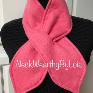 May include: A pink fleece neck warmer with a unique design and the text "NeckWearthyByLois" embroidered on the front.