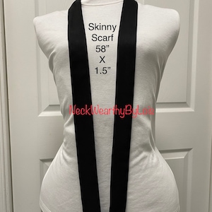 May include: A black skinny scarf, 58 inches long and 1.5 inches wide. The scarf is displayed on a white mannequin.